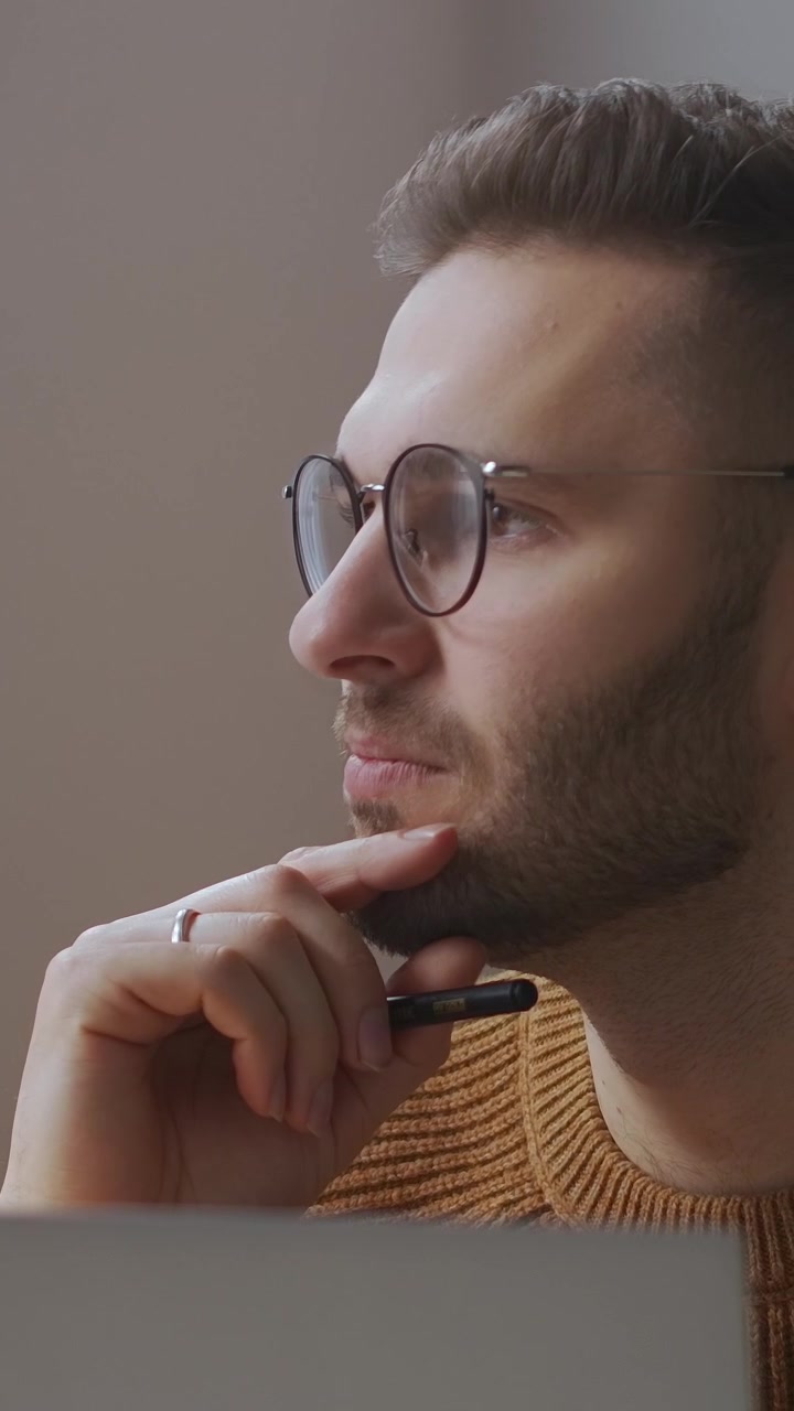 Giovane uomo pensieroso con gli occhiali che lavora al laptop