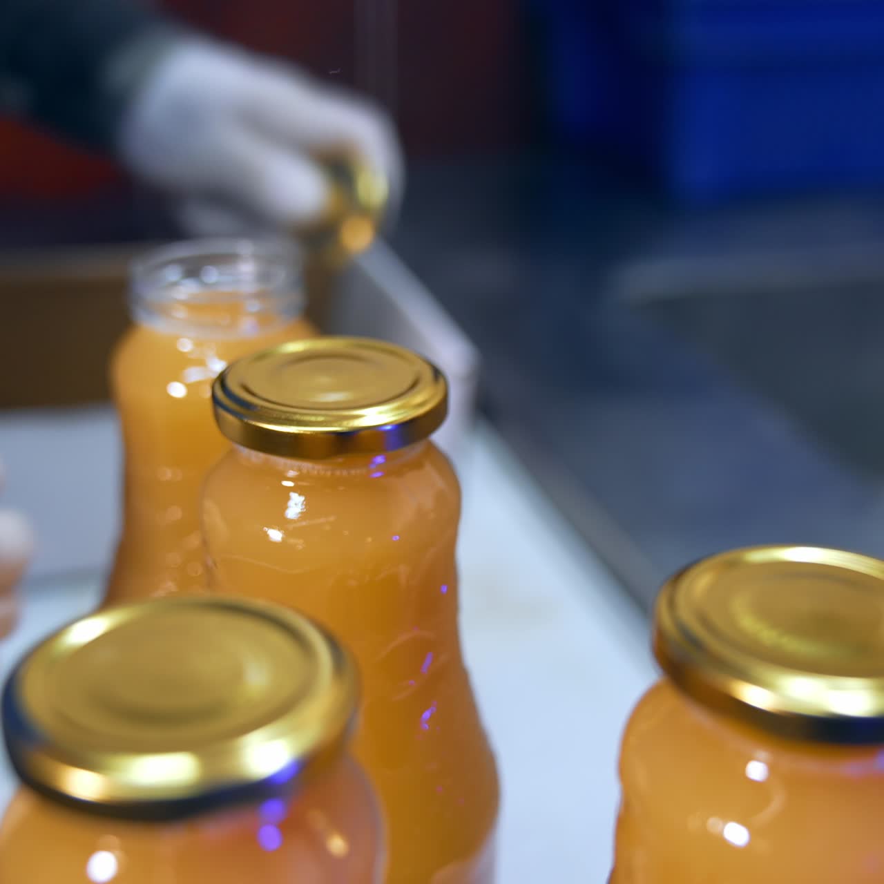 Food factory worker's hands in gloves put the caps on the bottles. Fresh apple juice in bottles being shut close up