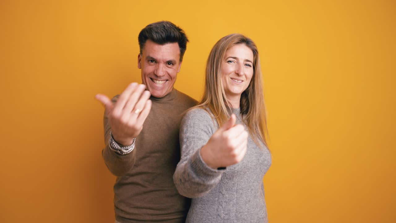 Coppia felice che invita gli spettatori con gesti delle mani su sfondo giallo