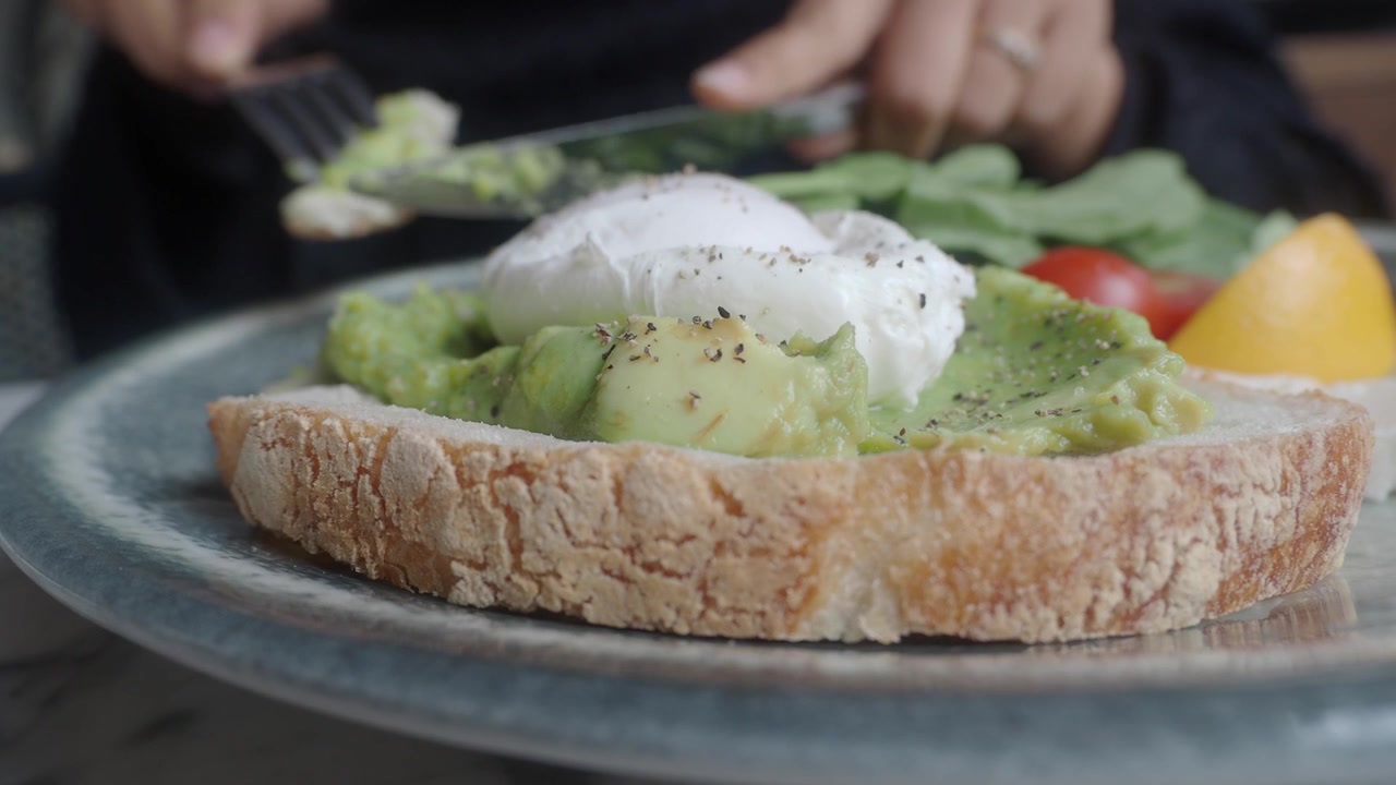 Persona che mangia avocado toast con uovo in camicia a colazione
