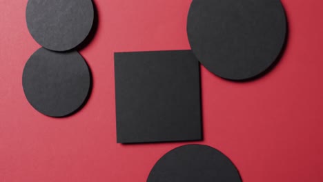 Video-of-close-up-of-square-and-circles-of-black-paper-and-copy-space-on-red-background