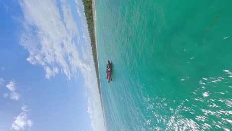 FPV-vertical-flight-over-green-colored-Caribbean-Sea-orbiting-boat-with-Dominican-republic-flag-in-sunlight