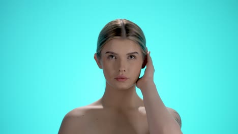 Medium-static-shot-of-a-young-woman-with-pretty-face-looking-charmingly-into-the-camera-and-running-her-hand-through-her-hair-in-front-of-turquoise-background-in-slow-motion