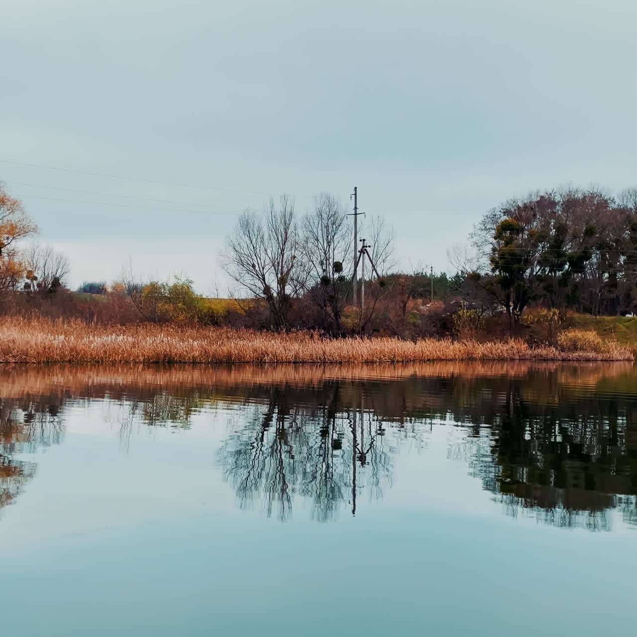 Narrow river with smooth calm surface in autumn. Leavings of old wooden footbridge peeping from water. Large metal bridge construction at backdrop