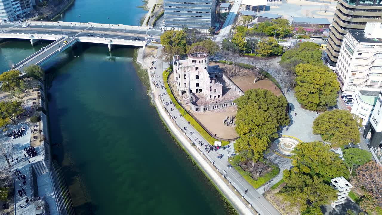 Paesaggio aereo da drone di turisti che camminano lungo il marciapiede del lungomare dell'edificio storico della Cupola Atomica Genbaku con il ponte Aioi sullo sfondo, fiume Motoyasu, città di Hiroshima, Giappone.
