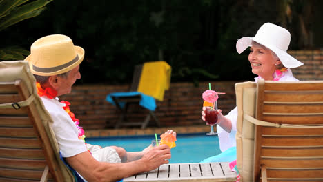 una pareja madura bebiendo cócteles junto a la piscina.