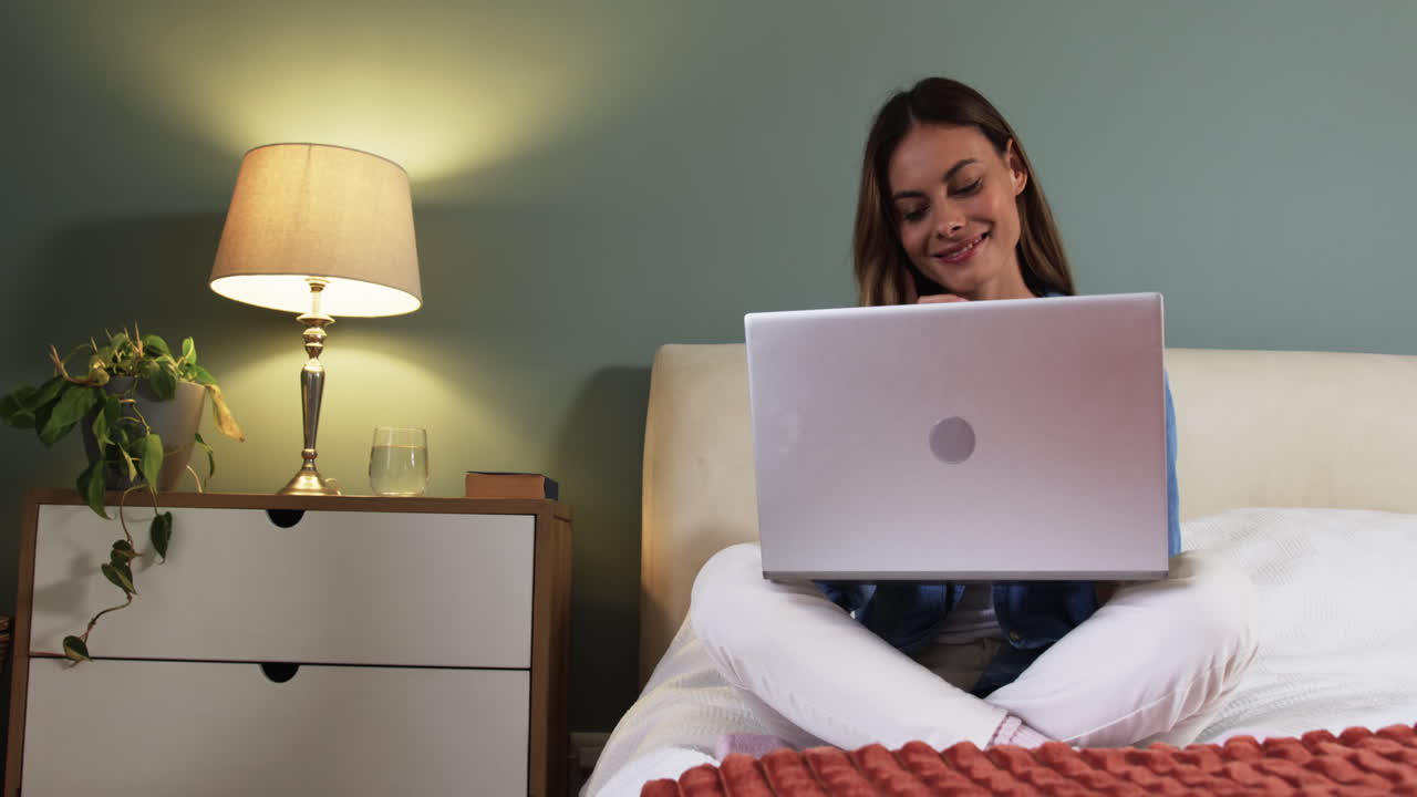 Relaxing at home, woman smiling while using laptop on cozy bed, copy space