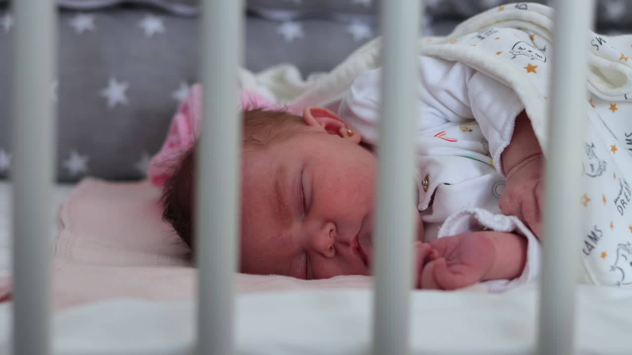 Scatto rubato all'altezza degli occhi attraverso le sbarre della culla di una neonata addormentata.