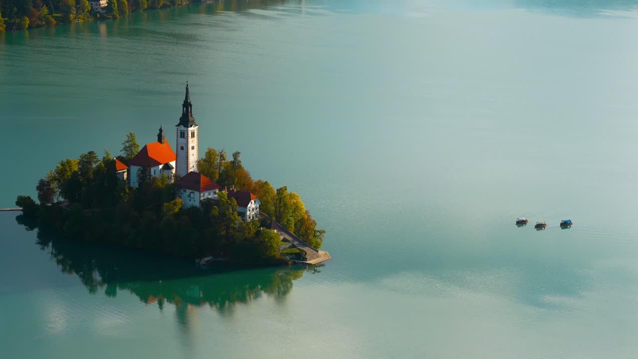 Le imbarcazioni Pletna scivolano verso la chiesa dell'isola di Bled sul tranquillo lago di Bled all'alba, zoom manuale in teleobiettivo