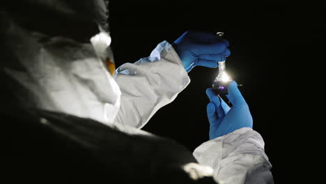 scientist in protective suit looks at a test tube with a drug