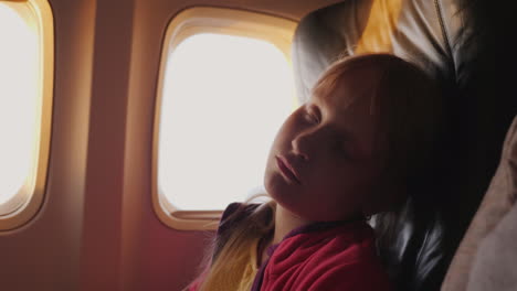 the little girl is sleeping in the cabin of the plane during the dawn the orange rays of the sun ill