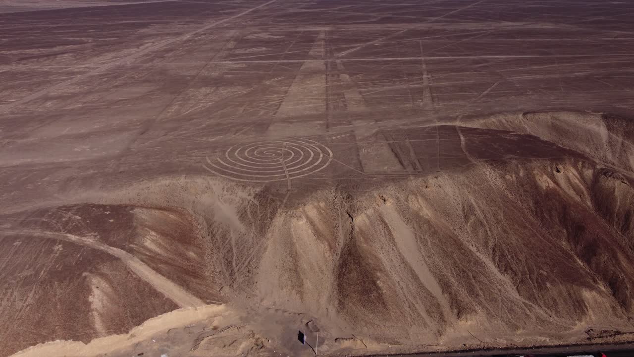 Aerial video of the Nazca Lines. Drone flies forward above the desert plateau tilting camera up. Below can be seen many long linear geoglyphs and a spiral symbol. Located in Nazca, Peru