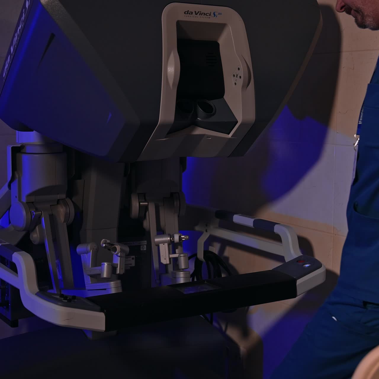 Male surgeon in blue uniform takes place in front of equipment. Specialist takes the handles of robotic device to rule the machine