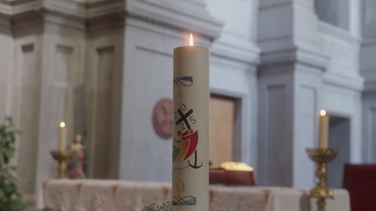 Primo piano di un cero pasquale acceso e decorato che brucia intensamente su un altare all'interno di uno sfondo sfocato di chiesa