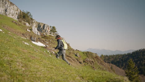 hiker with a light green backpack walking up a hill on the mountain, clear sky