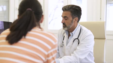 male doctor discussing reports on computer with female patient in clinic