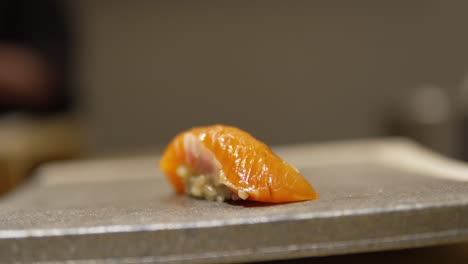 close-up of a fresh salmon sushi roll being placed on a tray for service