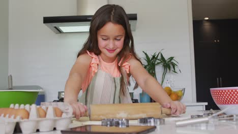 happy caucasian girl rolling dough for cookies in kitchen