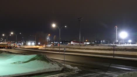 Pan-of-city-streets-with-busses-and-semi-trucks-passing,-night