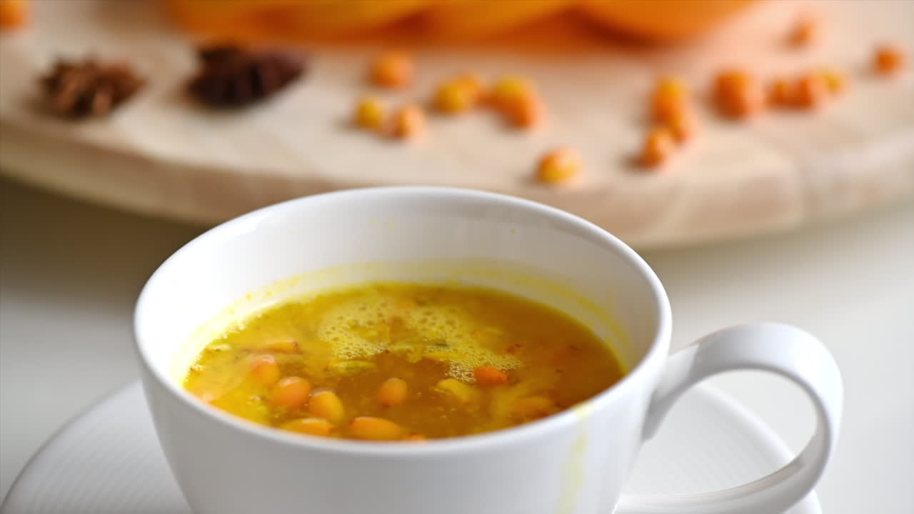 Sea buckthorn falling into a whit cup of tea, slow motion