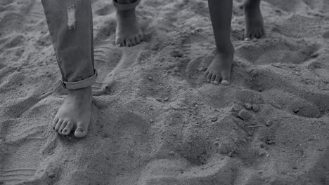 a black and white image of the feet of a child with his mother, walking on the beach