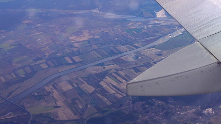 Vinduesudsigt til flyvinge over lappetæppe af spansk landbrugsland og snoet flod under klart dagslys.