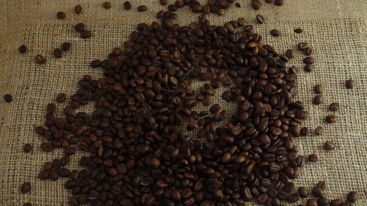 Chicchi di caffè cadono su tela di iuta al rallentatore.