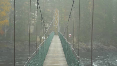 pov crossing suspended wooden bridge over violent turbulent river on a misty forest