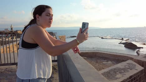 A woman is taking a picture of the ocean with her cell phone