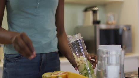 Midsectin of smiling african american attractive woman preparing smoothie in kitchen