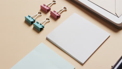 primer plano de cuadernos, bolígrafos y papelería dispuestos sobre un fondo beige, en cámara lenta
