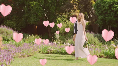 animación de corazones rosados sobre una feliz pareja diversa caminando en un jardín soleado el día de la boda