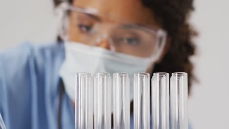 Video-of-biracial-female-doctor-with-face-mask-using-pipette-on-blue-background