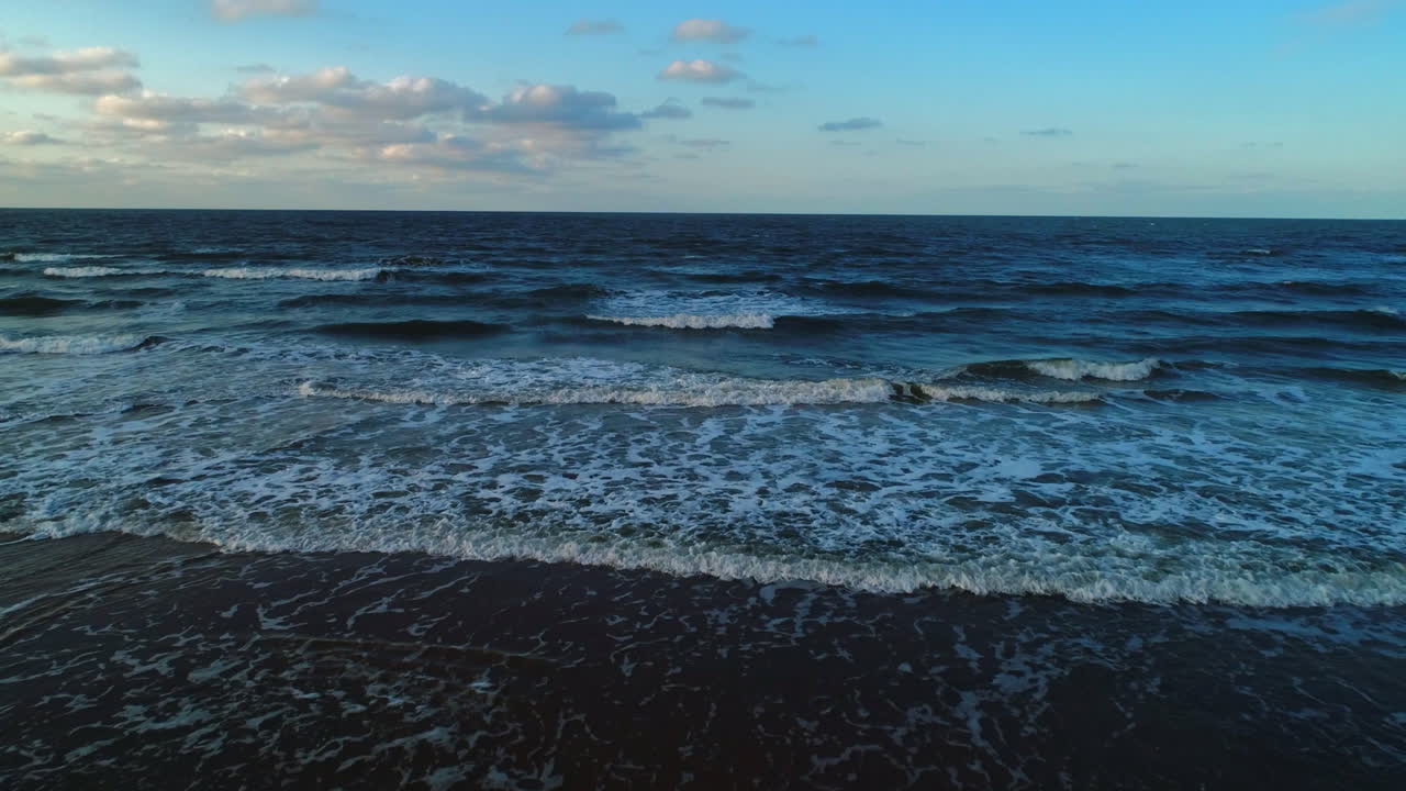 Low Front On Aerial Drone Shot Flying into the Sea from Sany Beach with Small Waves Breaking and clear Horizon with Sunny and Cloudy Sky at Sunrise Sunset