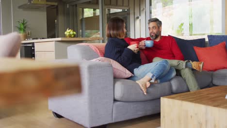 pareja feliz diversa sentada en la sala de estar bebiendo café y hablando