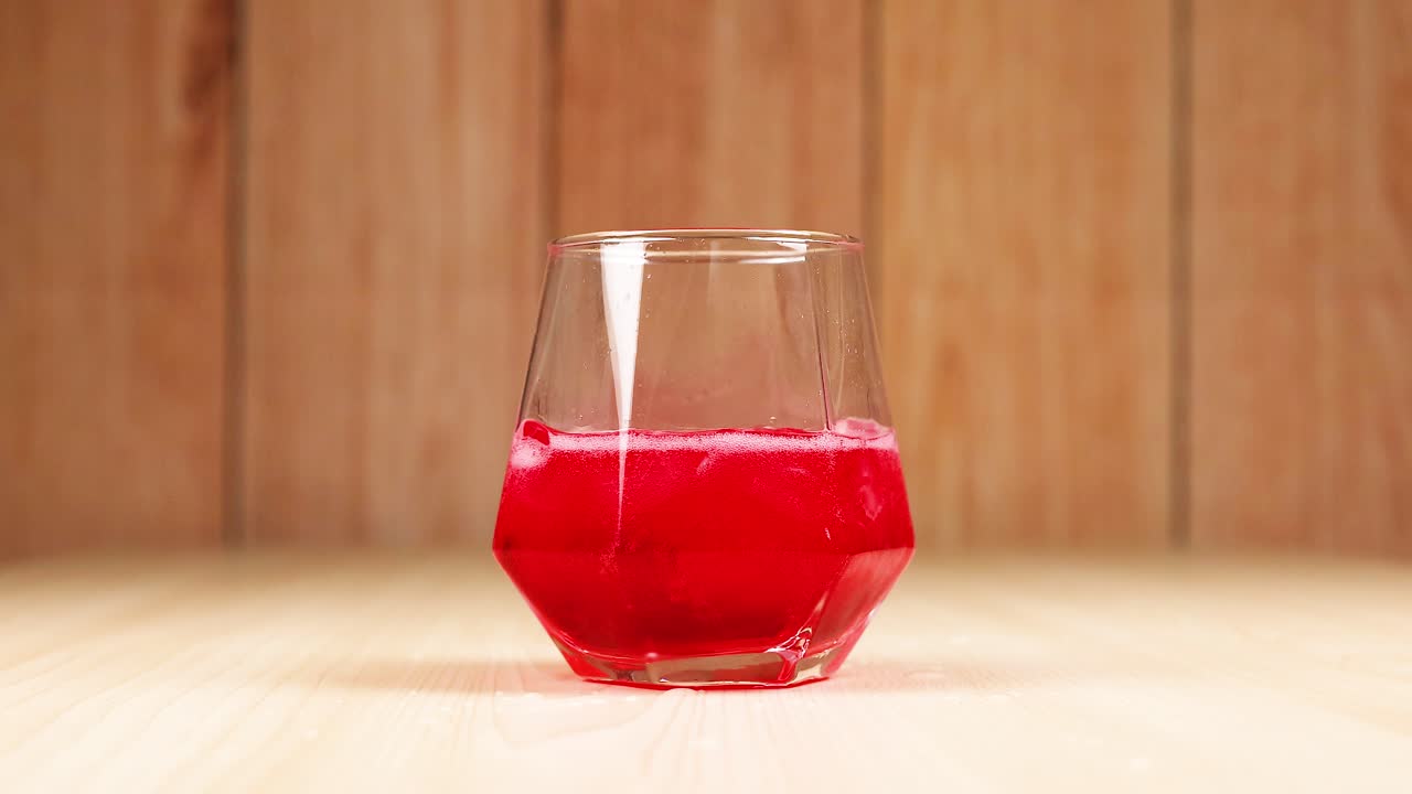 Red drink poured into glass with ice