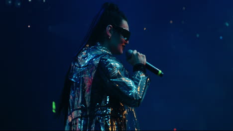 woman with long black hair sings into microphone on a stage in front of a crowd