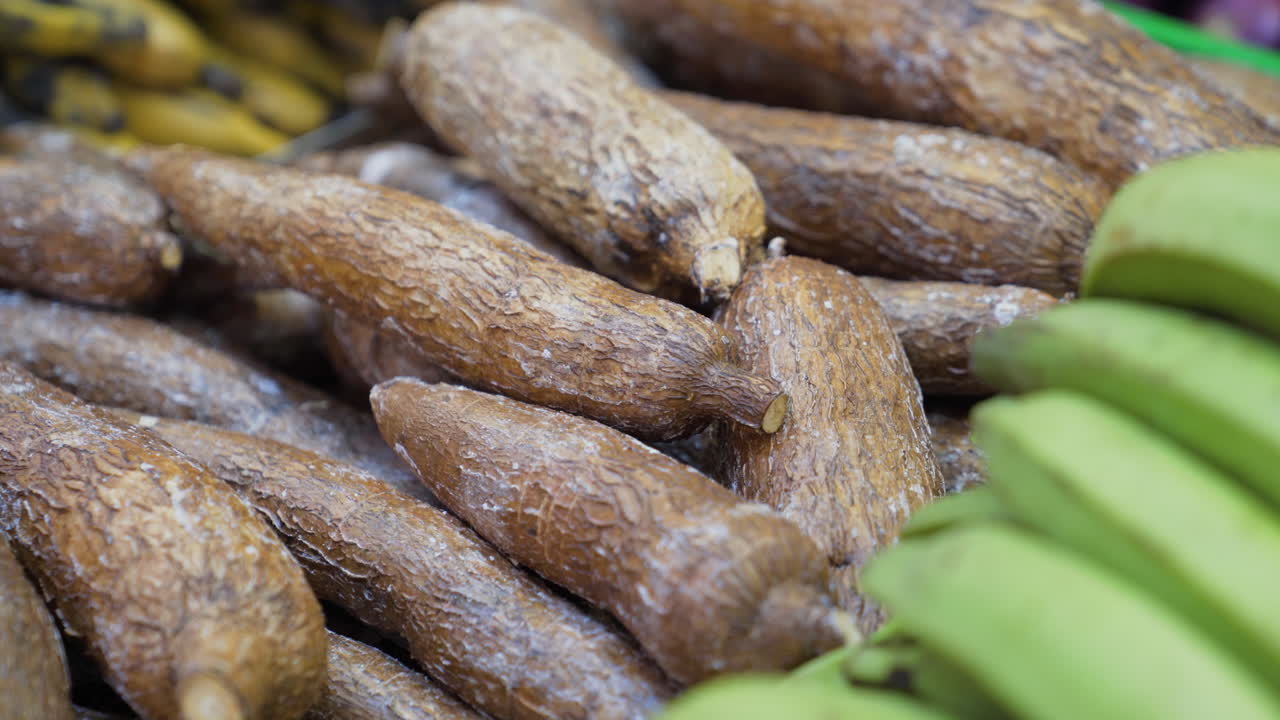 A pile of fresh cassava roots displayed on a market stall, showcasing their rough texture and natural appeal in a food market setting.