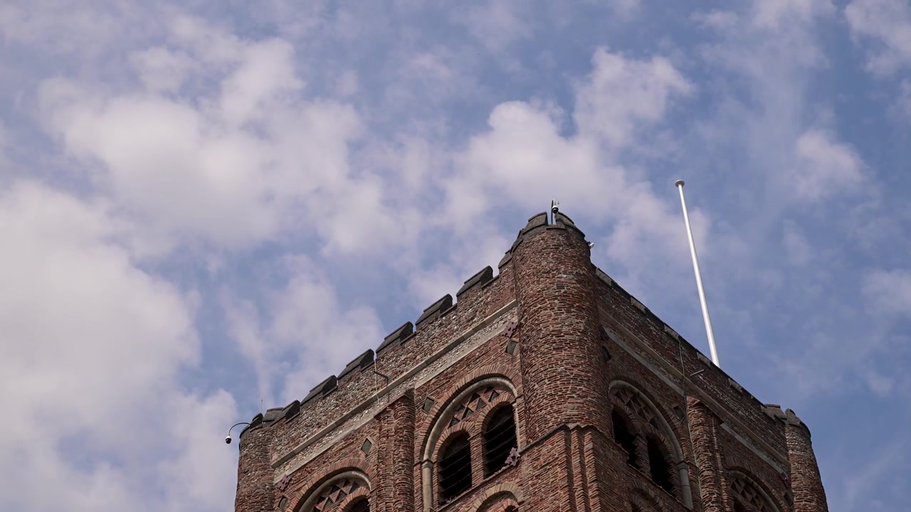 La torre in mattoni della Cattedrale di St Albans si erge in un cielo blu mentre nuvole leggere passano sopra l'inquadratura