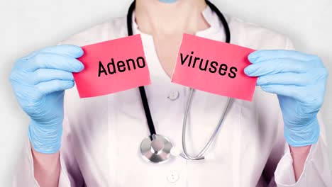 primer plano, manos con guantes médicos azules sujetan y rasgan una tarjeta de papel rojo con una inscripción adenovirus. médico vestido con uniforme médico blanco, tiene un estetoscopio