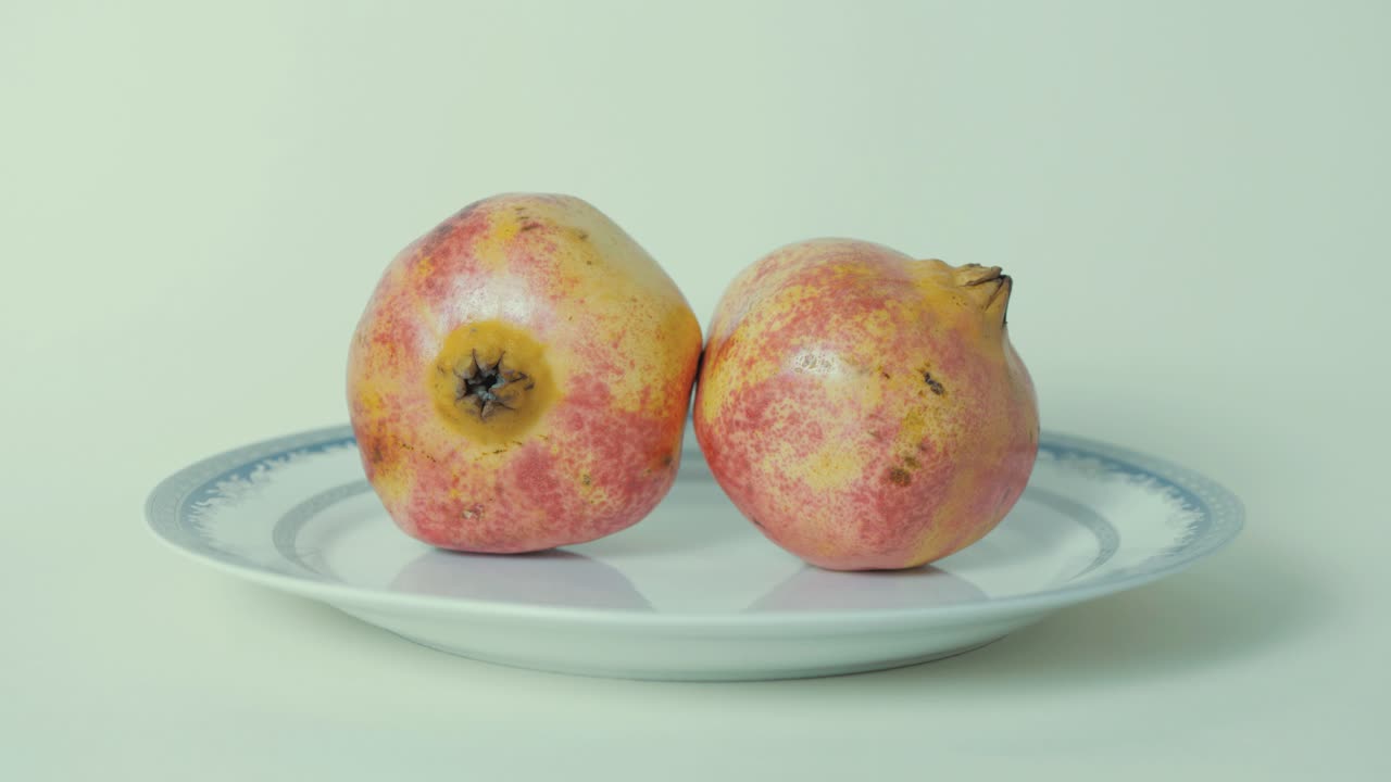 Frutto di melograno maturo su piatto su sfondo bianco.