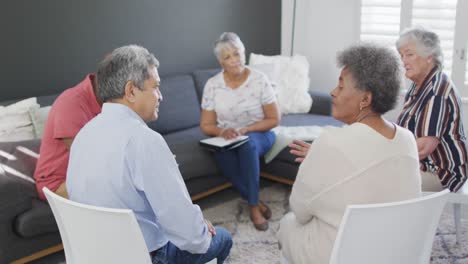 Mixed-race-senior-female-counsellor-with-clipboard-advising-to-group-of-diverse-senior-friends