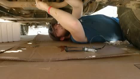 static shot of a man lies under truck doing repairs on a bright hot day