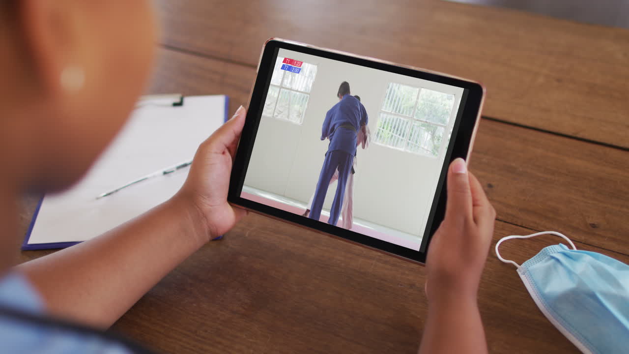 태블릿에서 유도 경기를 보는 얼굴 마스크로 테이블에 앉아 있는 여성의 합성