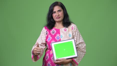 mature beautiful indian woman showing digital tablet and giving thumbs up