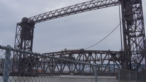 vertical-lift-style-bridge-in-the-Cleveland-Flats-on-the-Cuyahoga-river,-Ohio-through-chain-link-fence