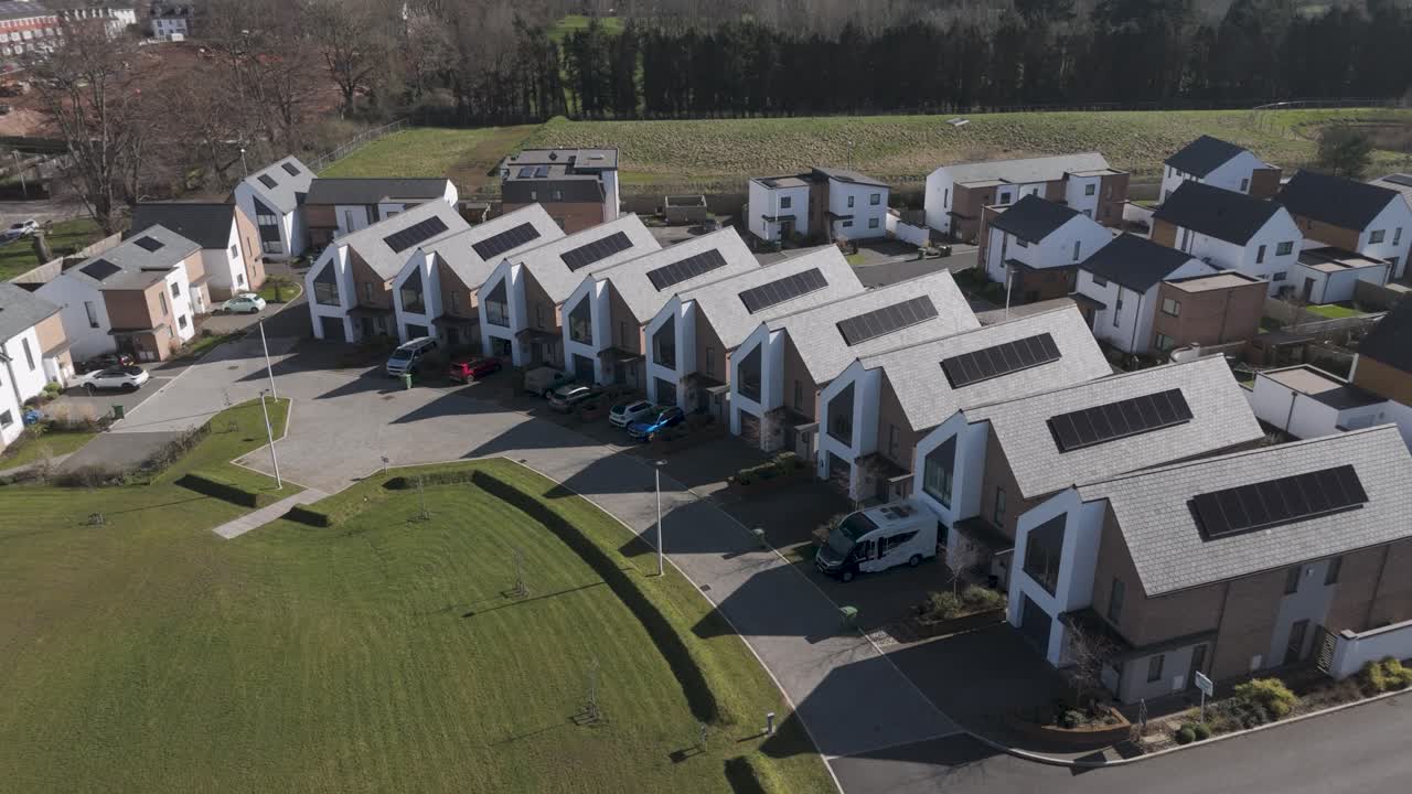Aerial sweep of gable-front solar townhouses curving around central lawn depicting community-oriented sustainable estate design