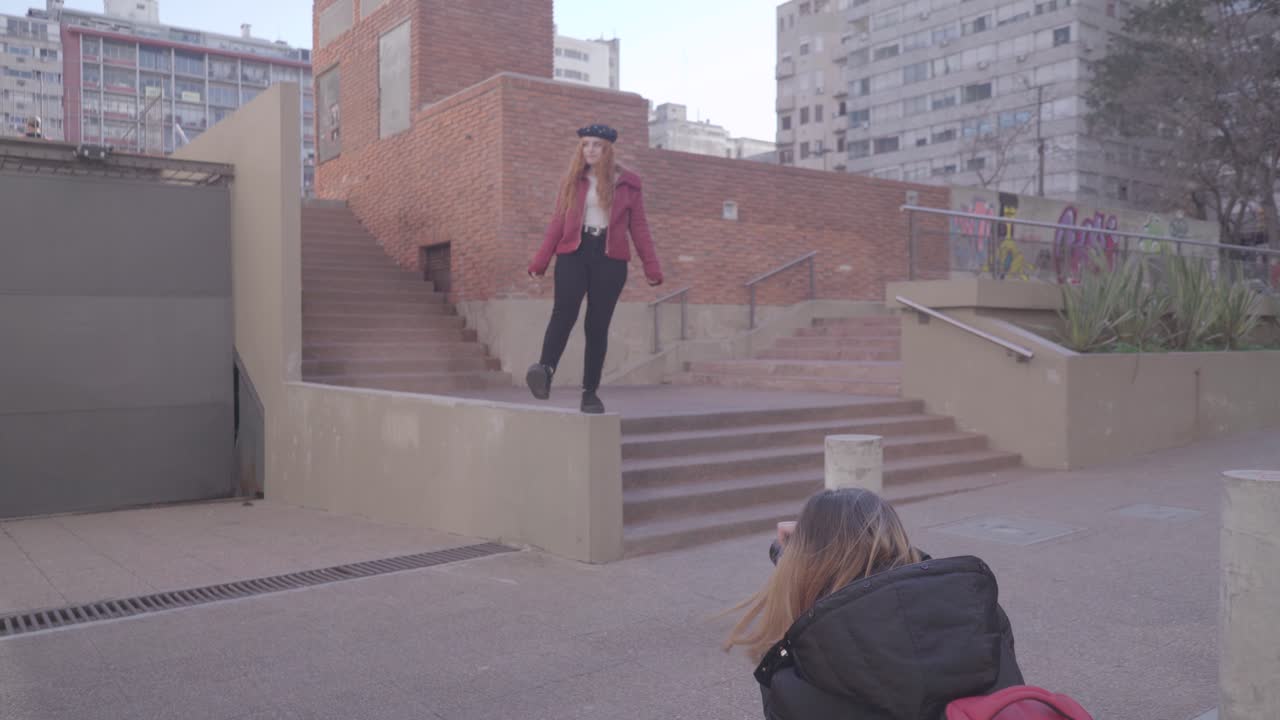 Two friends have fun taking pictures in the street. Redheaded model makes a creative poses and smiles for her photographer friend