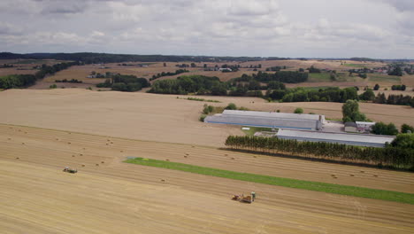 up drone aerial shot over wide filed during harvesting in poland - tractor and people working with straw cubes