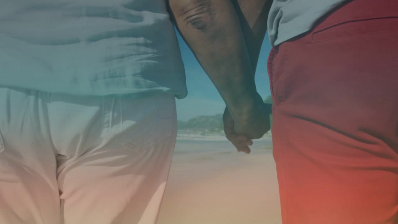 Couple walking on coastal beach, low-angle camera following hands and showing flare for travel